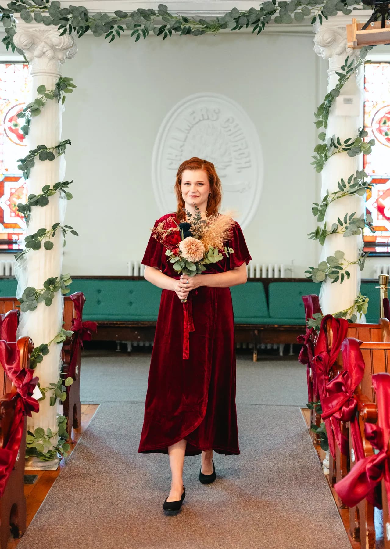 Bridesmaids in burgundy dresses with bouquets inside the church at Kody and Jaz’s wedding.
