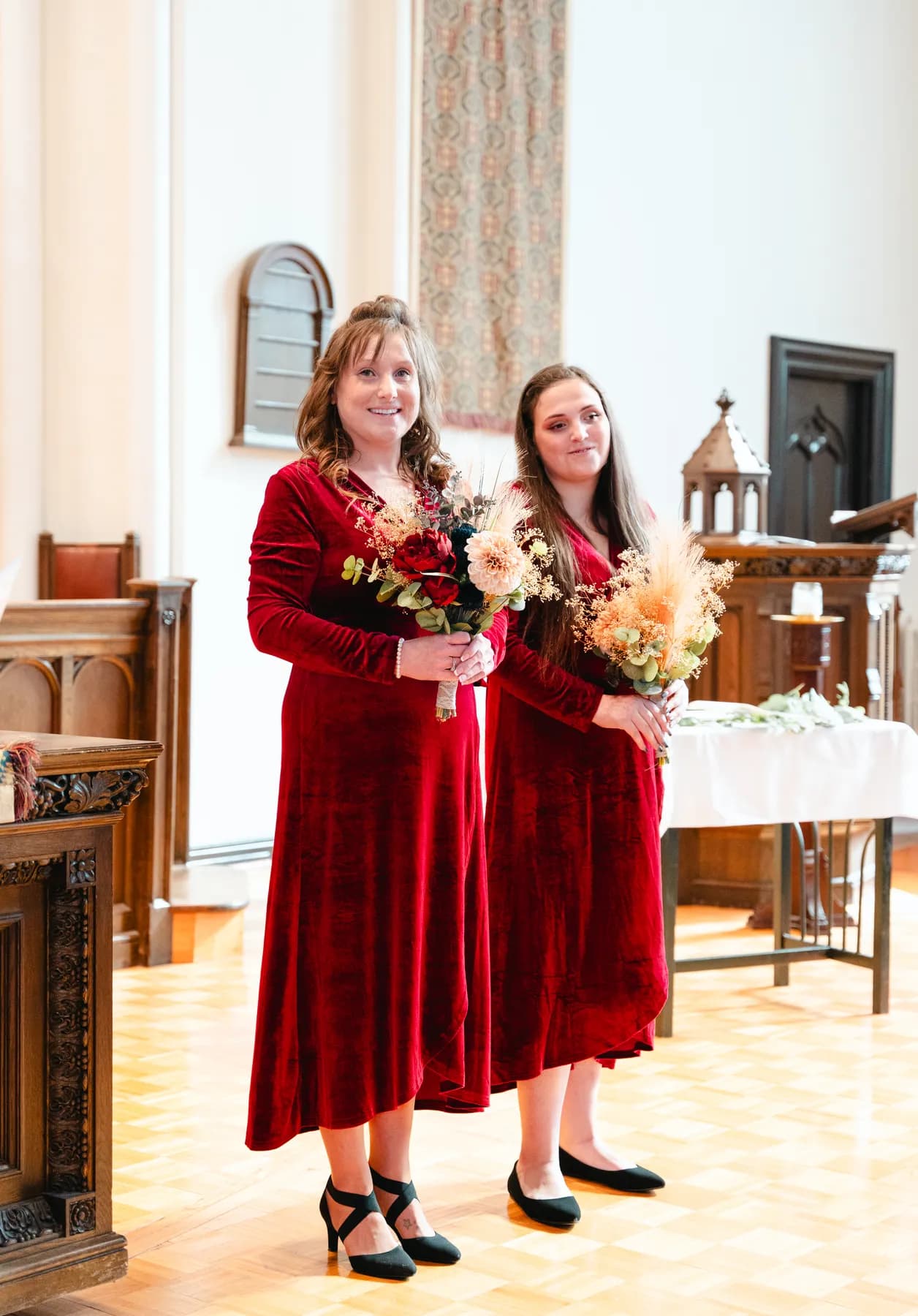 Bridesmaids in burgundy dresses with bouquets inside the church at Kody and Jaz’s wedding.