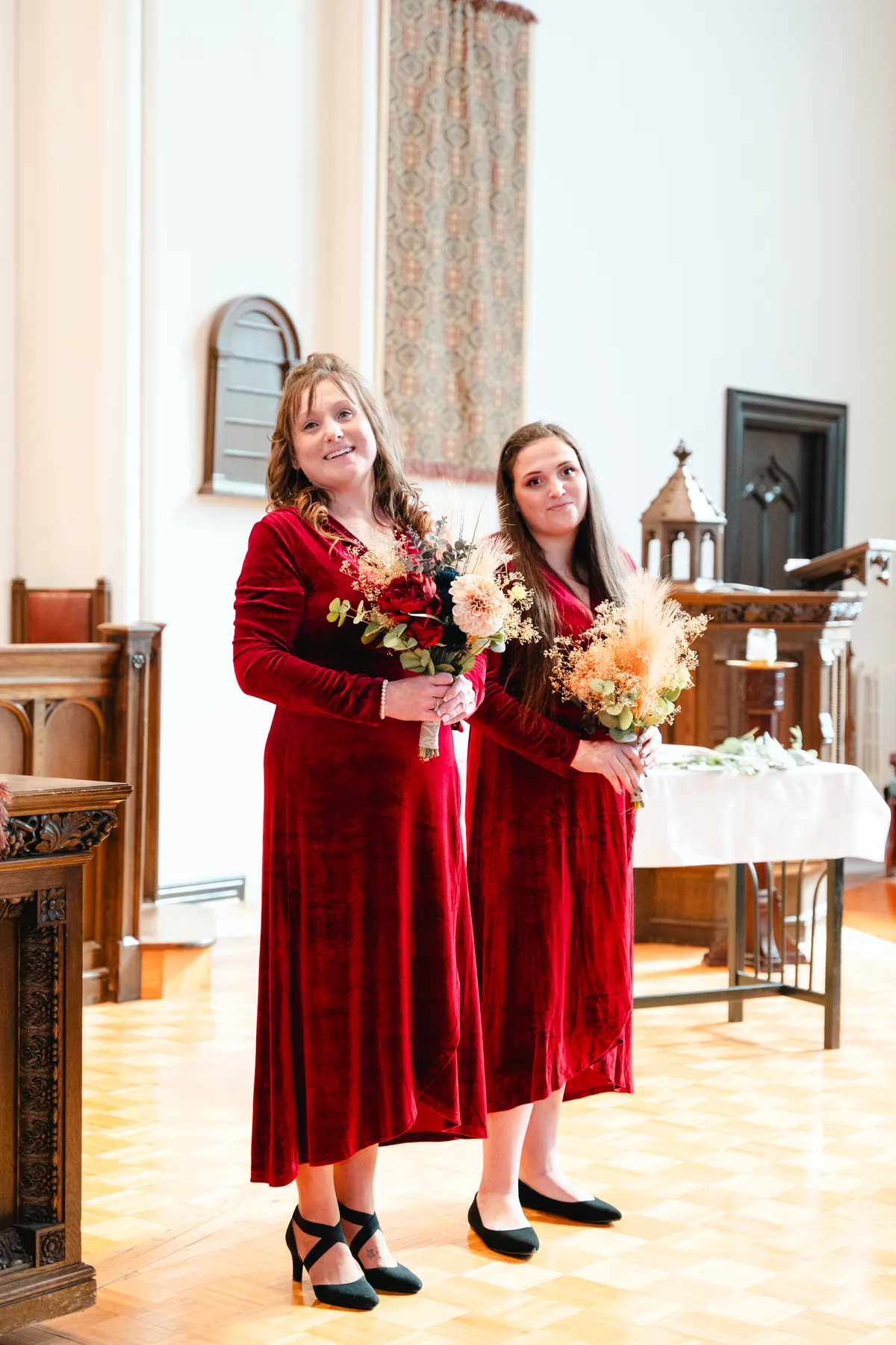 Bridesmaids in burgundy dresses with bouquets inside the church at Kody and Jaz’s wedding.