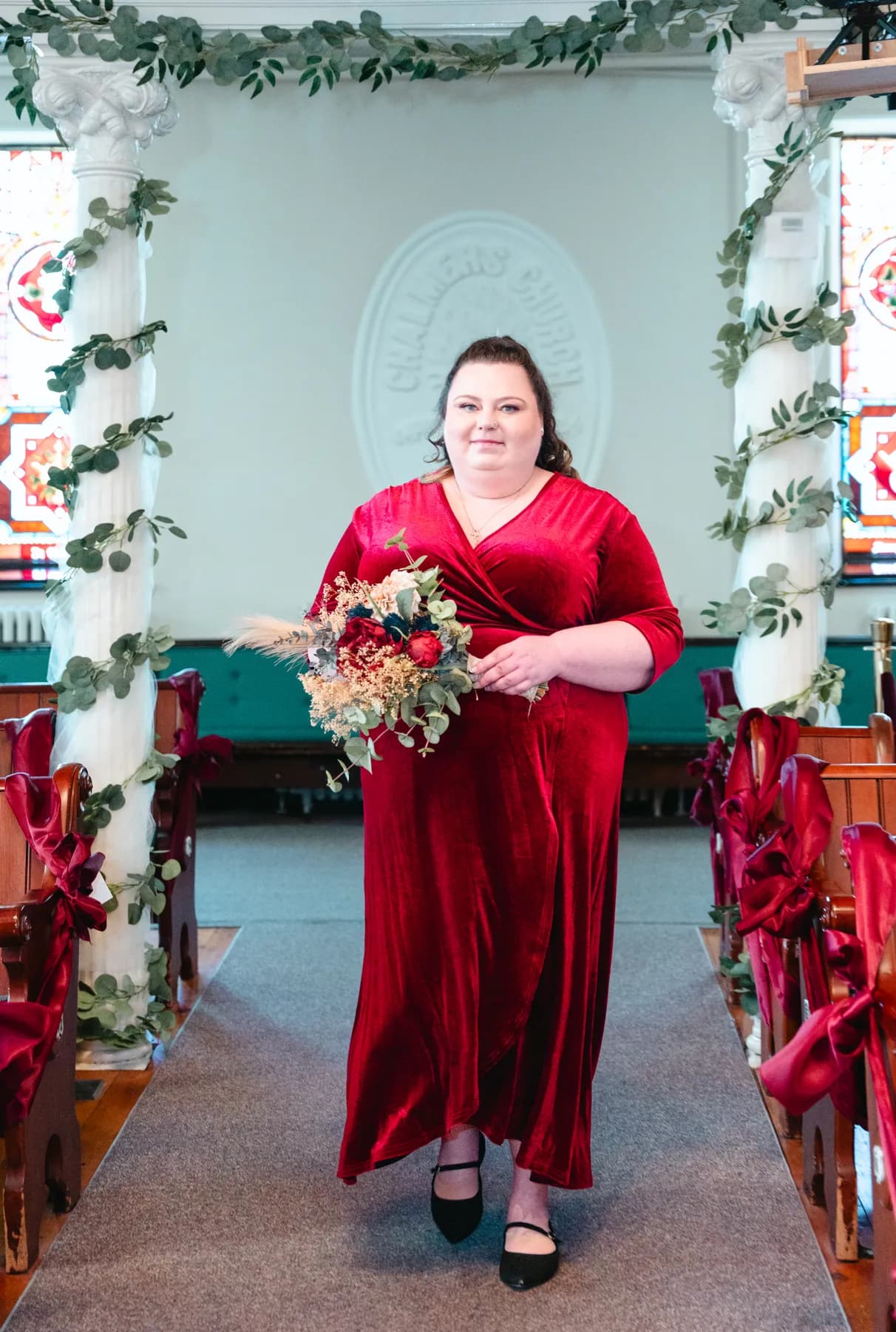 Bridesmaids in burgundy dresses with bouquets inside the church at Kody and Jaz’s wedding.