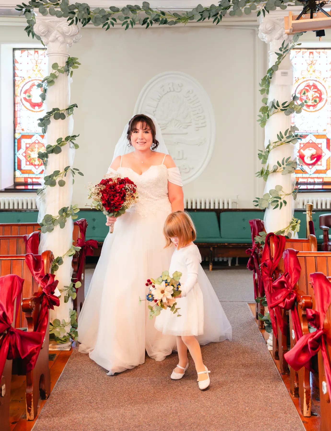 The bride with a flower girl at the front of the church at Kody and Jaz’s wedding.