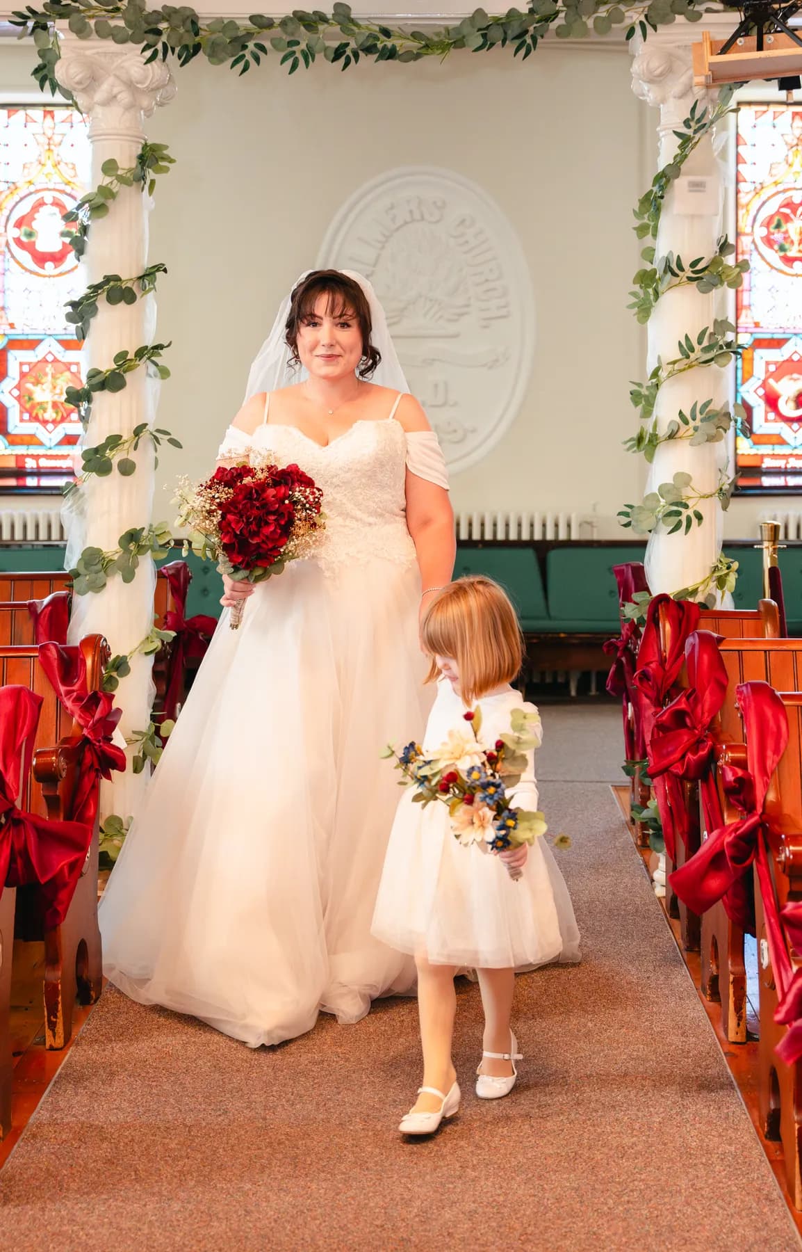 The bride with a flower girl at the front of the church at Kody and Jaz’s wedding.