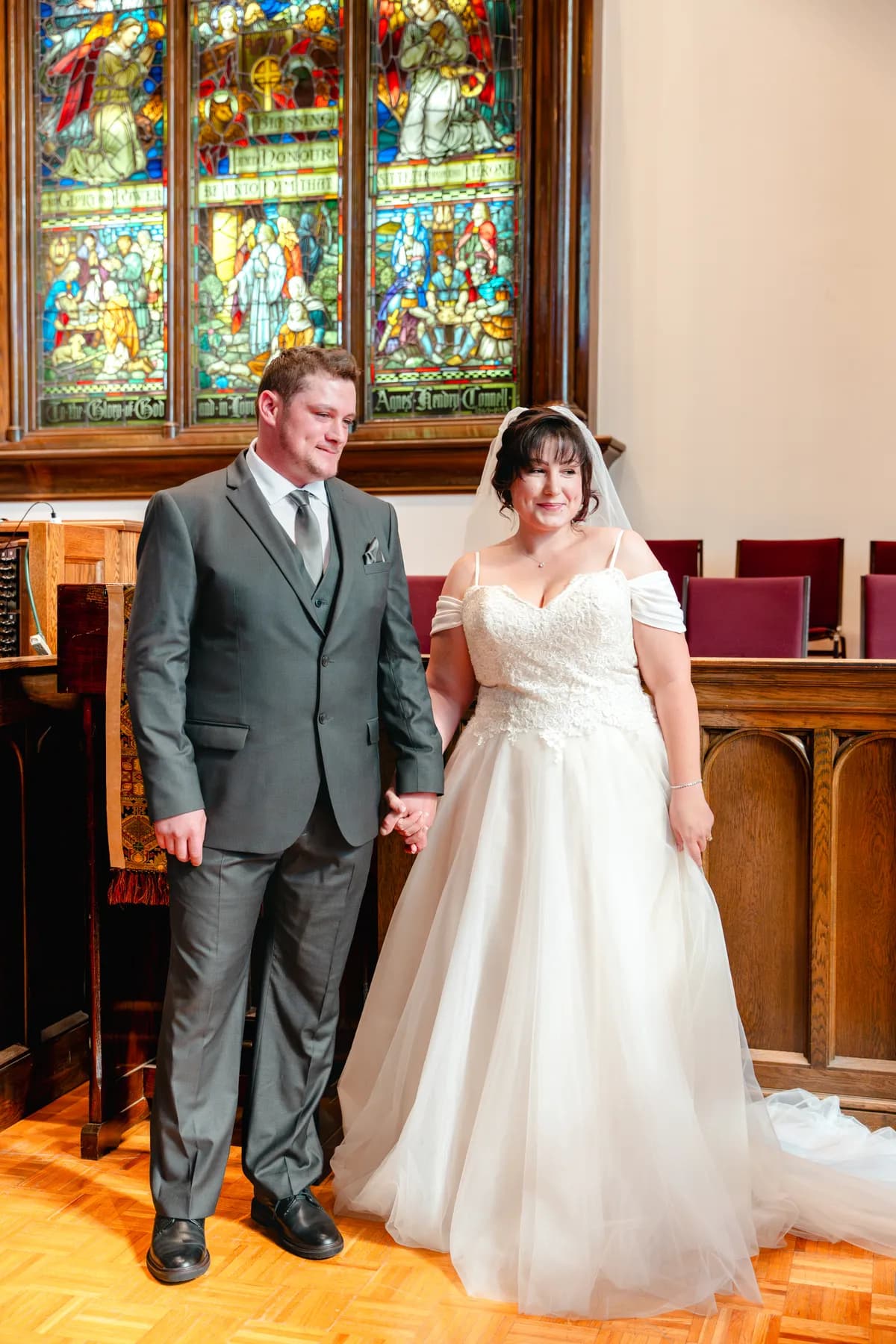 The newly married couple beside stained glass windows at Kody and Jaz’s wedding.