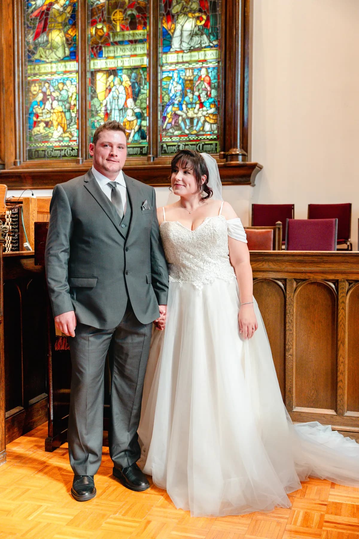The newly married couple beside stained glass windows at Kody and Jaz’s wedding.