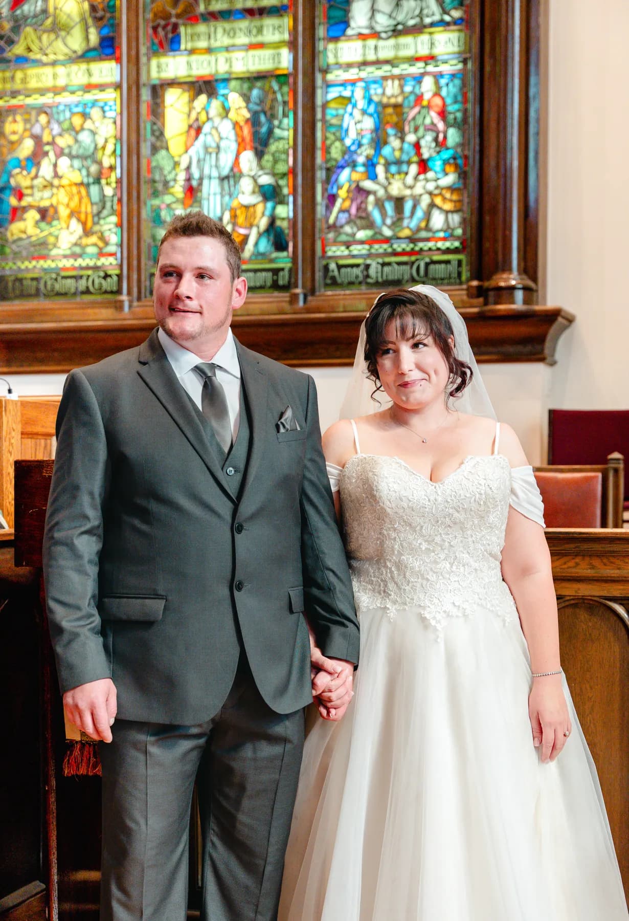 The newly married couple beside stained glass windows at Kody and Jaz’s wedding.