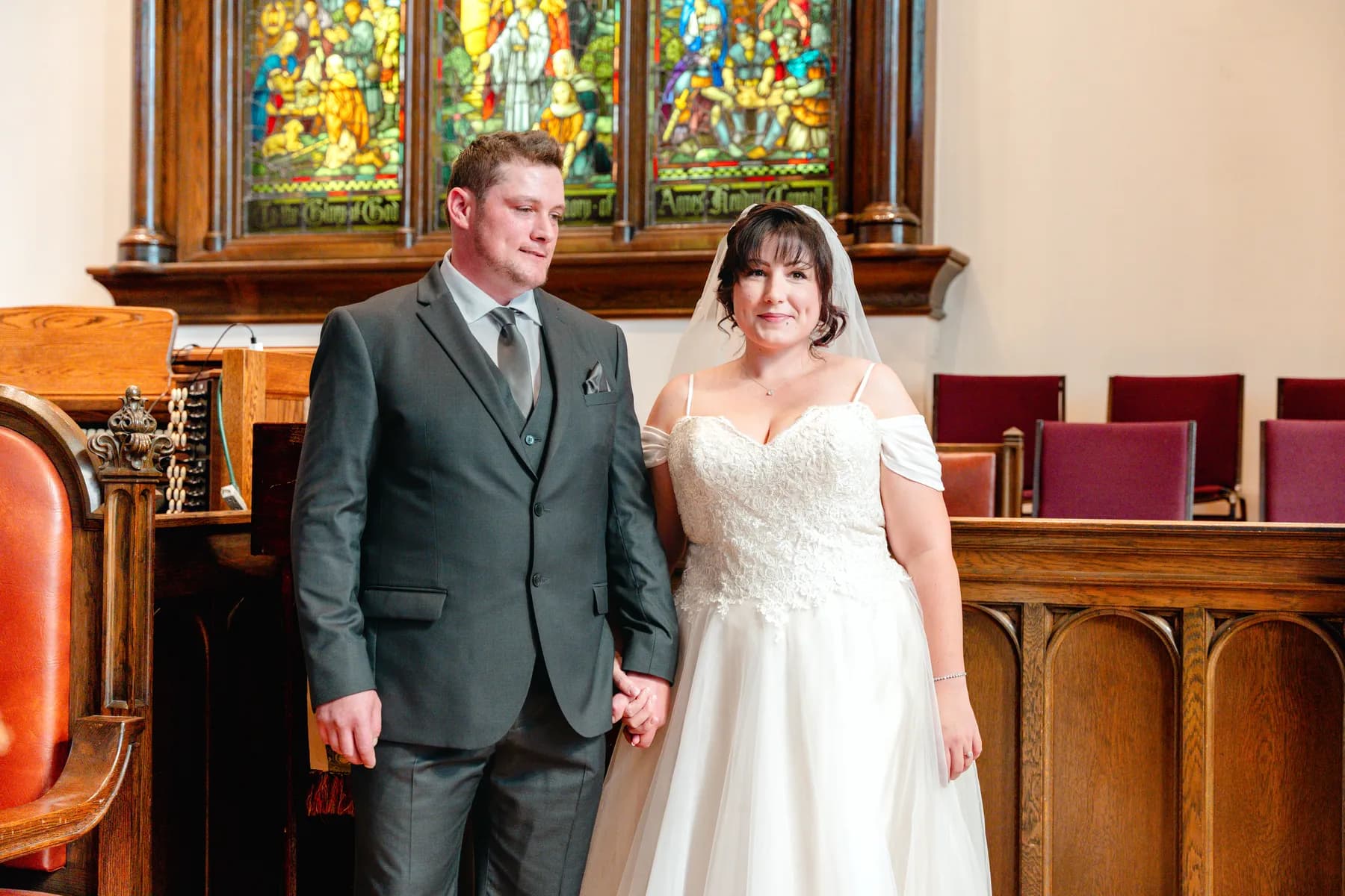 The newly married couple beside stained glass windows at Kody and Jaz’s wedding.