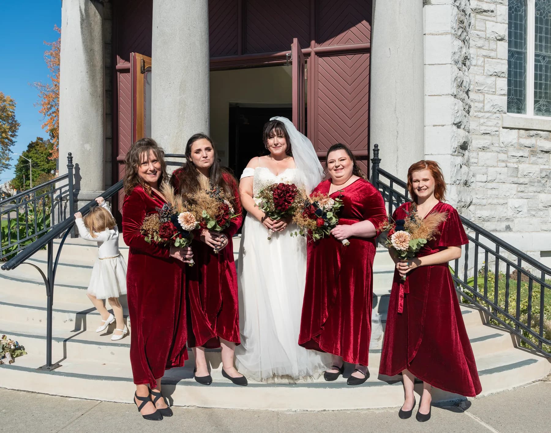 The bride with bridesmaids and a flower girl outside the church at Kody and Jaz’s wedding.