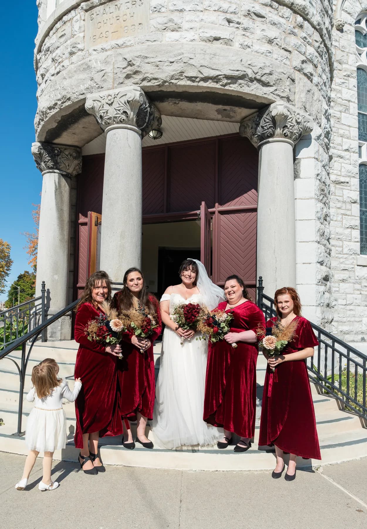 The bride with bridesmaids and a flower girl outside the church at Kody and Jaz’s wedding.