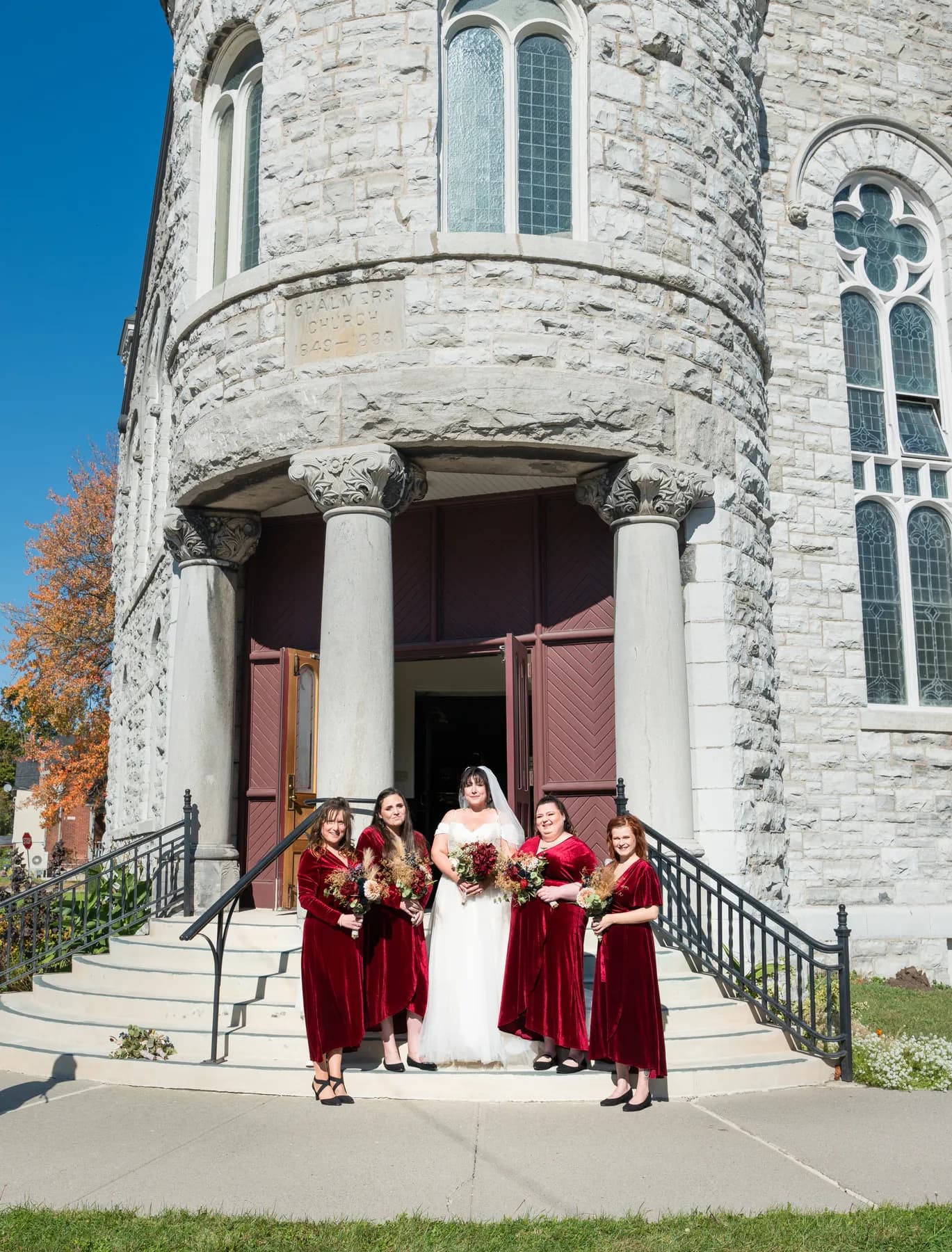 The bride with bridesmaids and a flower girl outside the church at Kody and Jaz’s wedding.