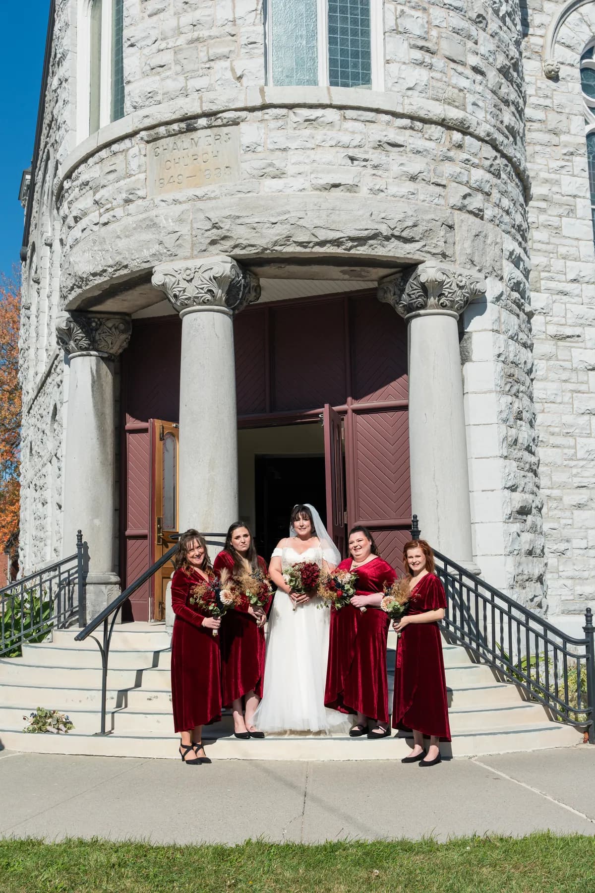 The bride with bridesmaids and a flower girl outside the church at Kody and Jaz’s wedding.