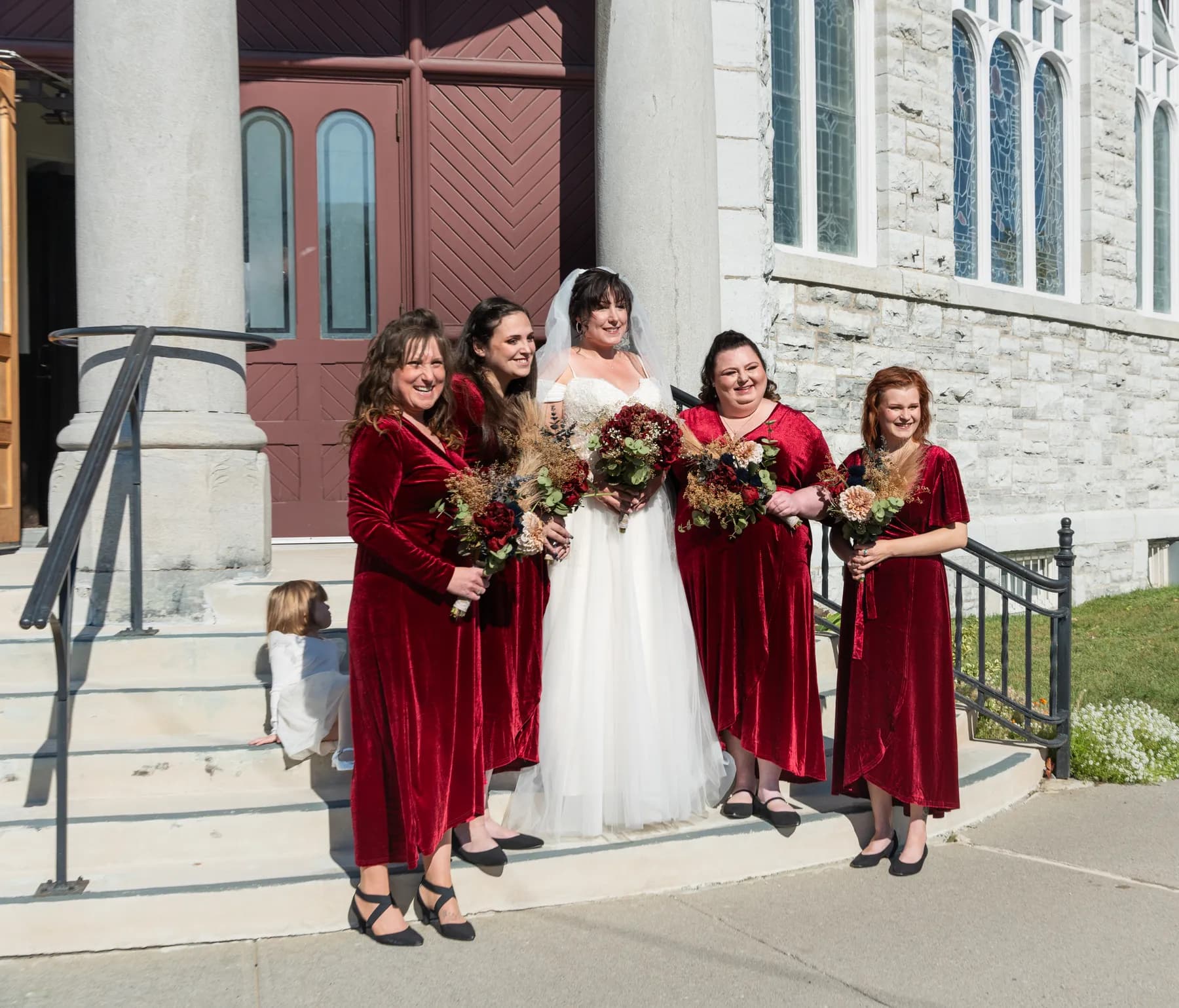 The bride with bridesmaids and a flower girl outside the church at Kody and Jaz’s wedding.