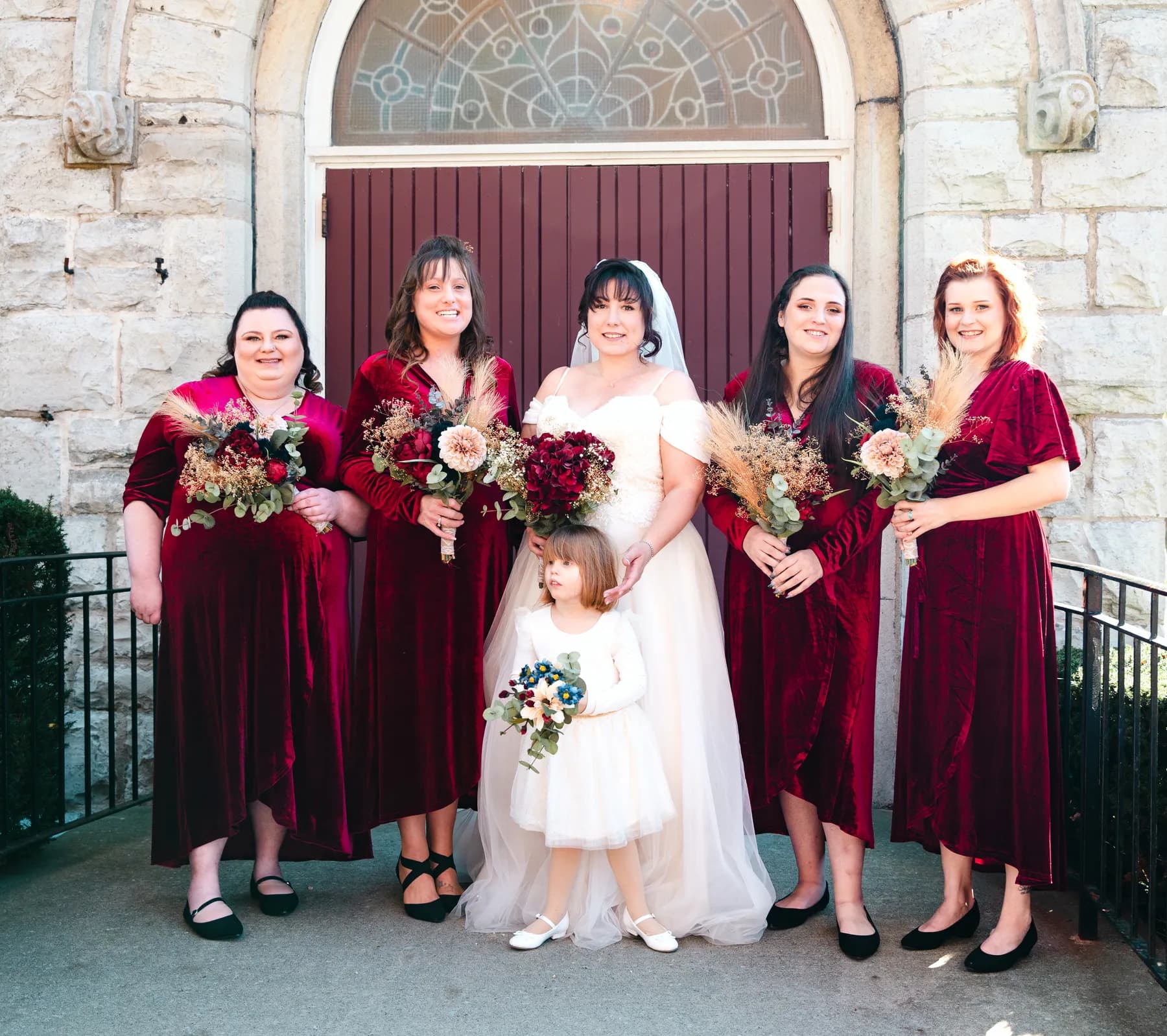 The bride with bridesmaids and a flower girl at the church door at Kody and Jaz’s wedding.
