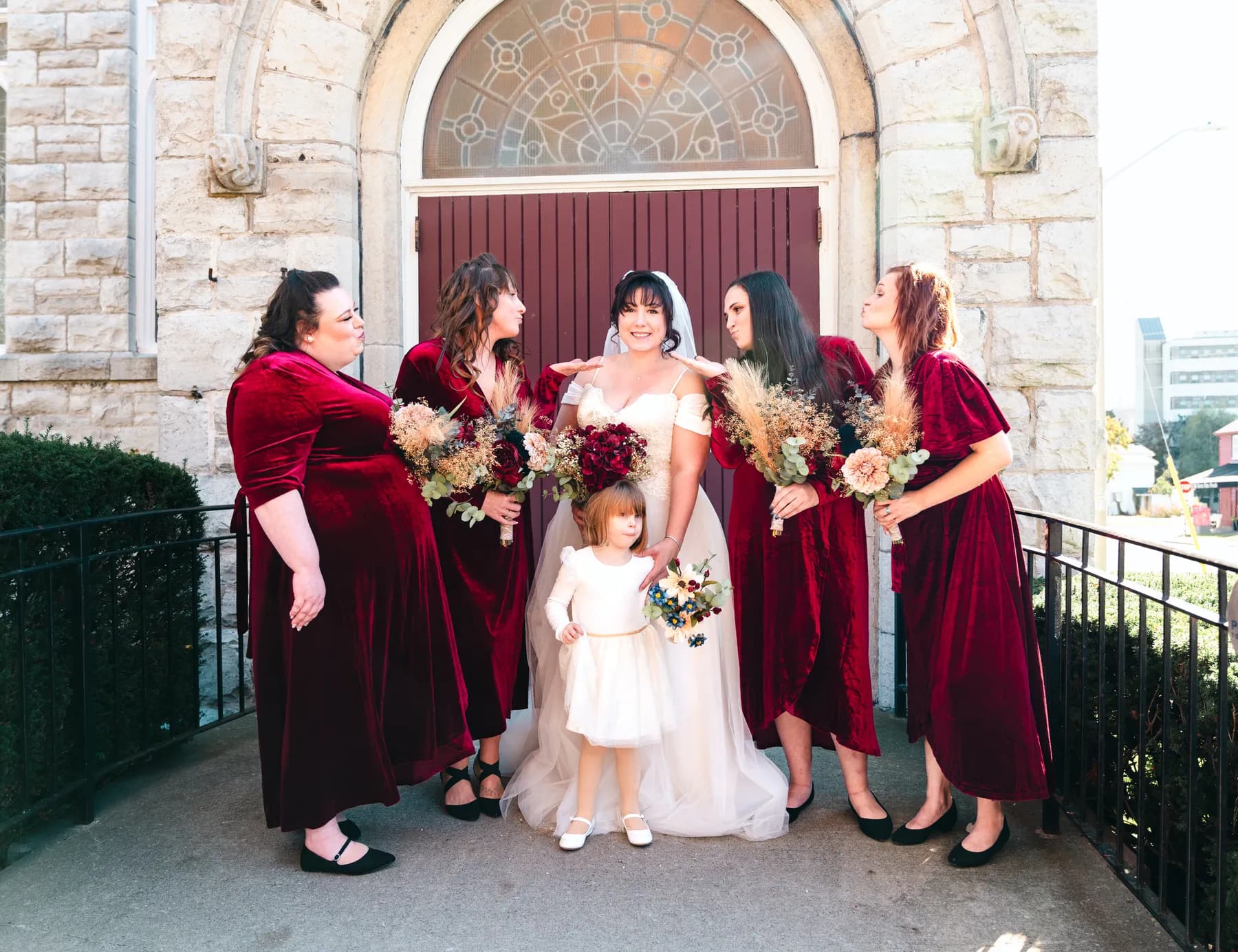 The bride with bridesmaids and a flower girl at the church door at Kody and Jaz’s wedding.