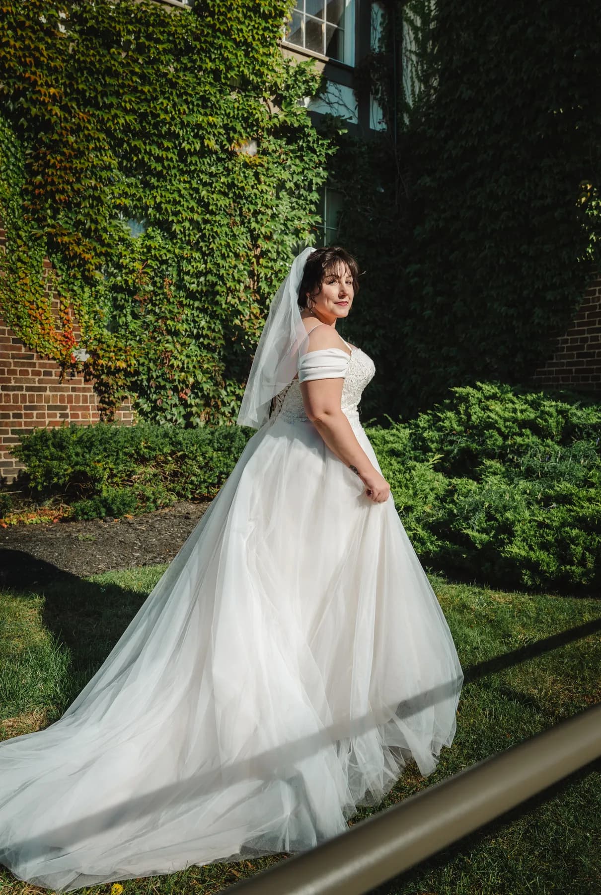 The bride posing in a garden with her gown trailing behind at Kody and Jaz’s wedding.