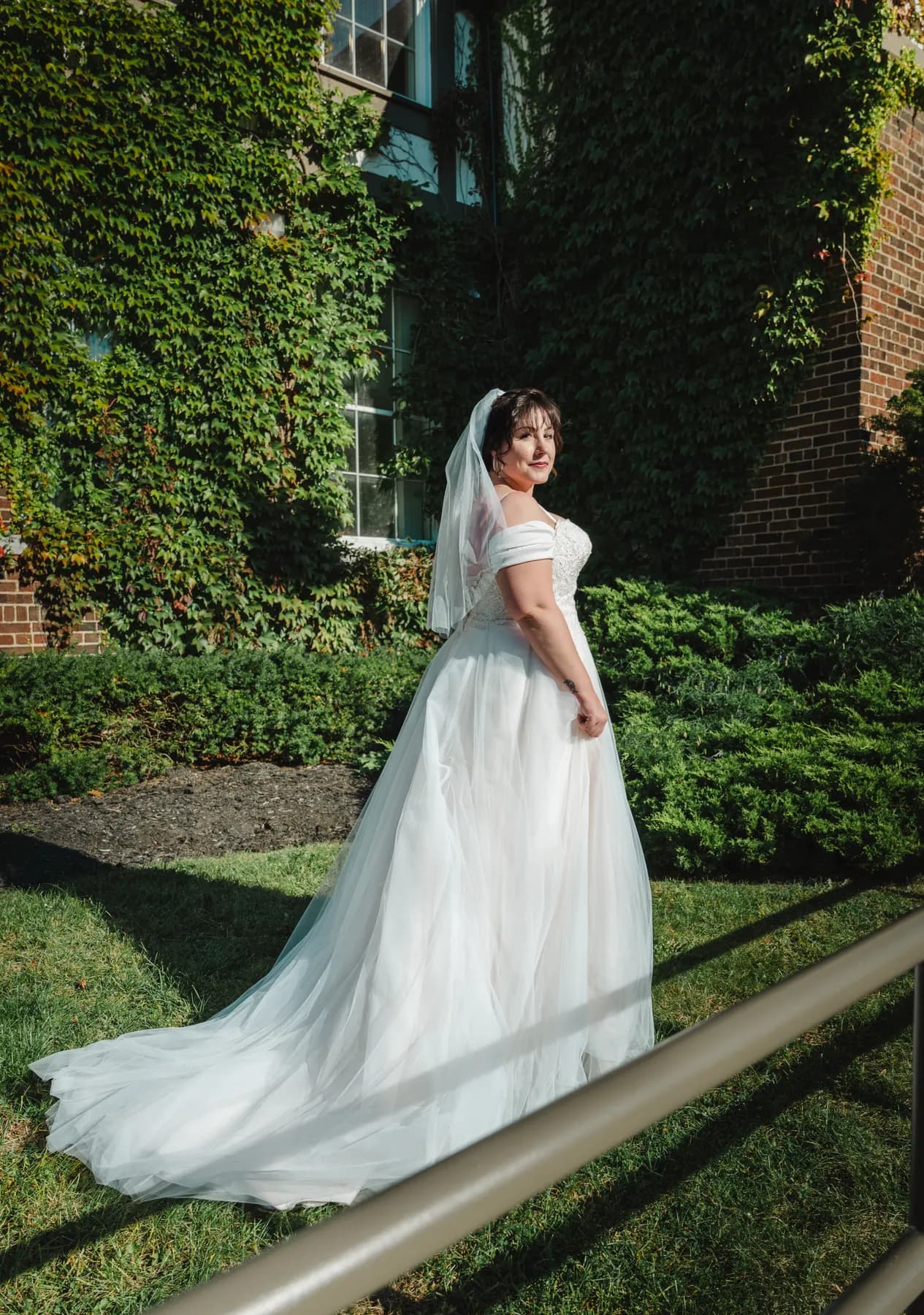The bride posing in a garden with her gown trailing behind at Kody and Jaz’s wedding.