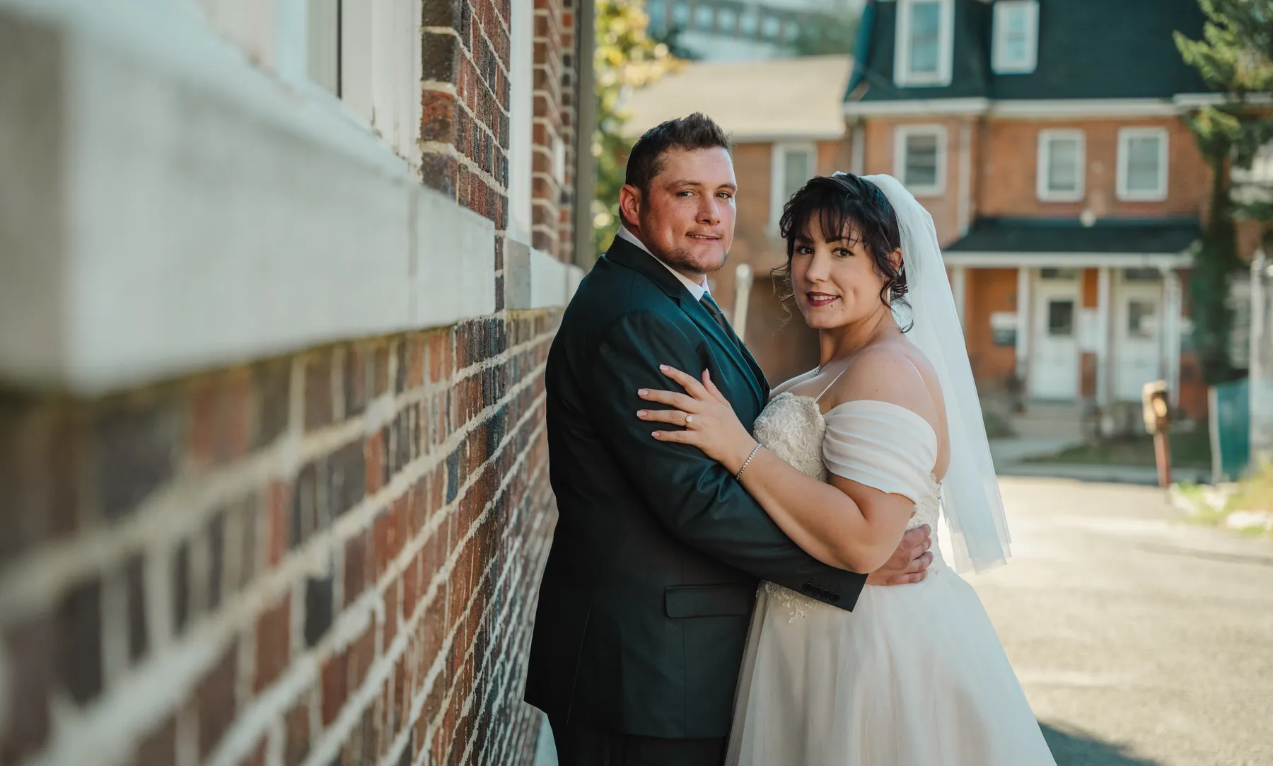The couple embracing beside a brick building at Kody and Jaz’s wedding.