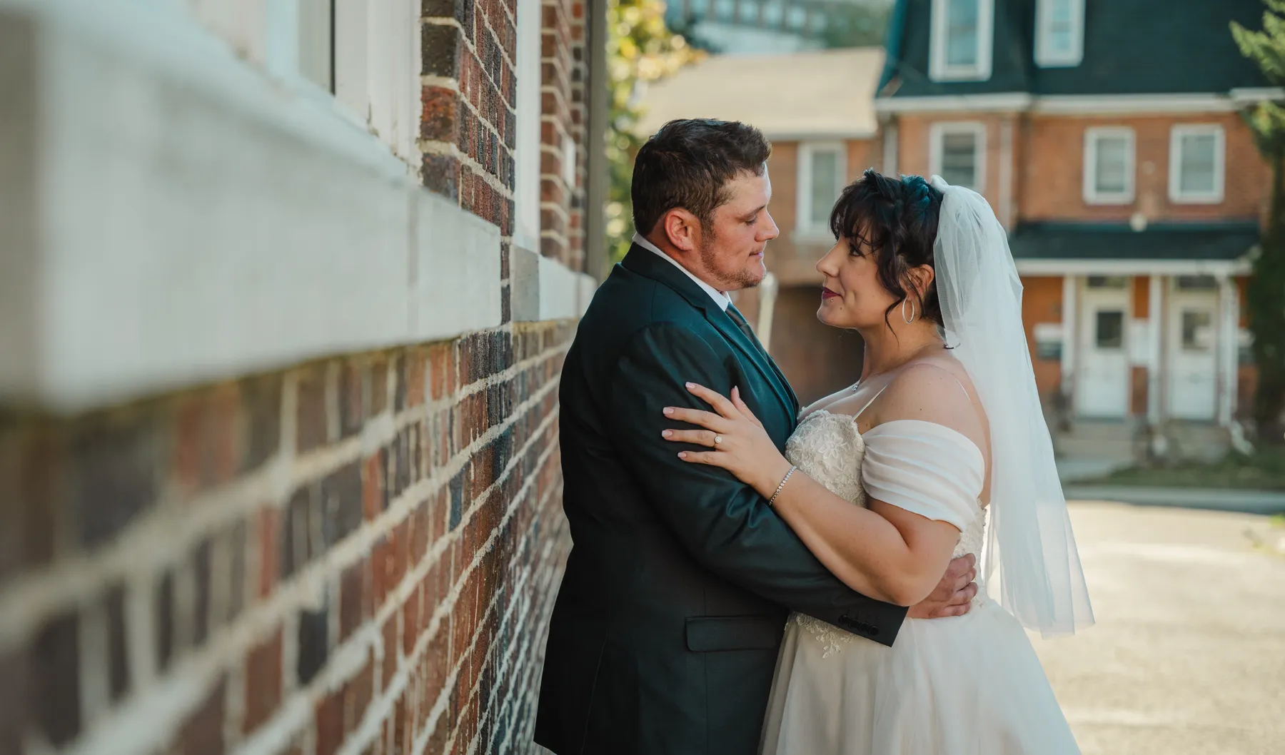 The couple embracing beside a brick building at Kody and Jaz’s wedding.