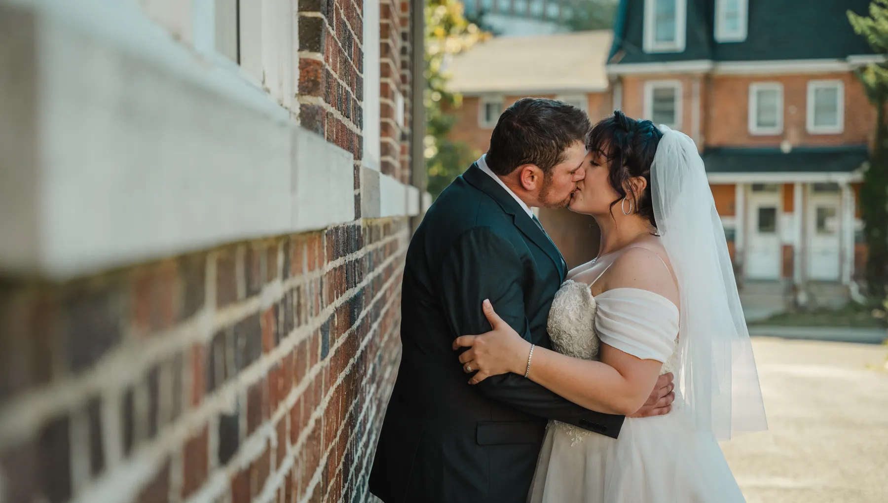 The couple embracing beside a brick building at Kody and Jaz’s wedding.