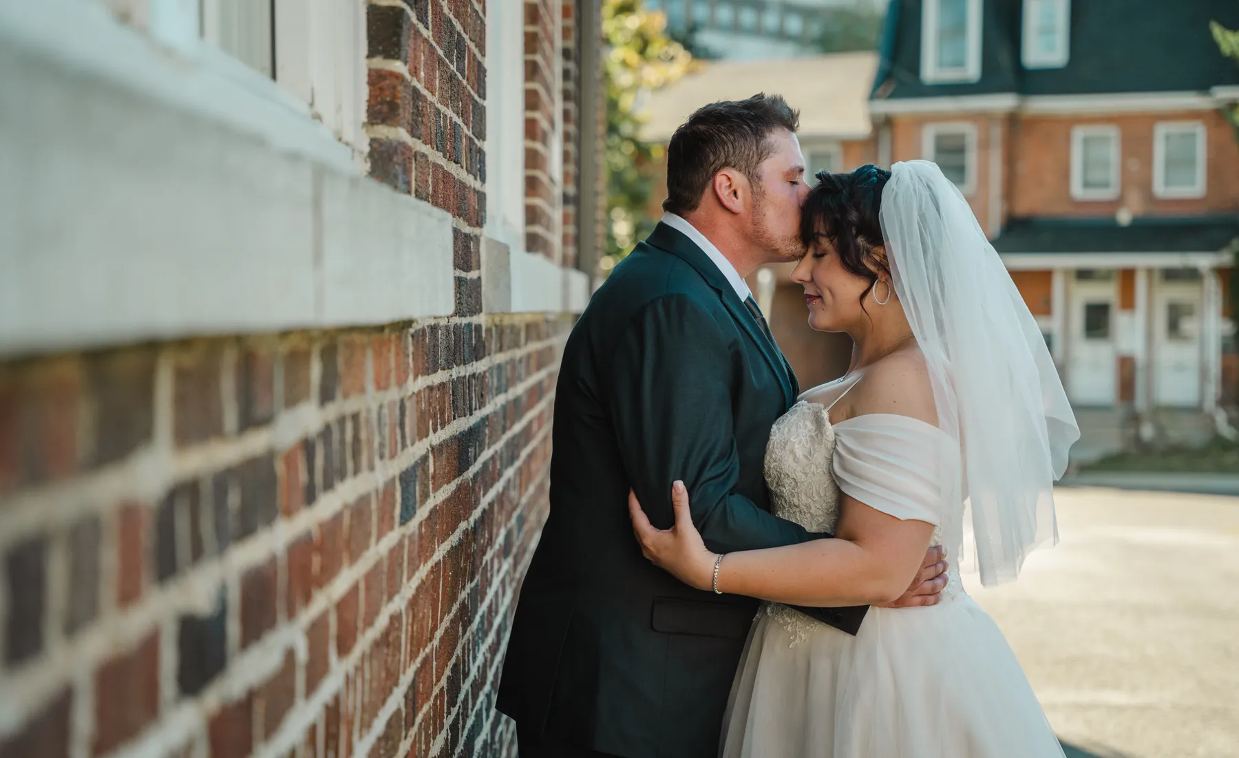 The couple embracing beside a brick building at Kody and Jaz’s wedding.