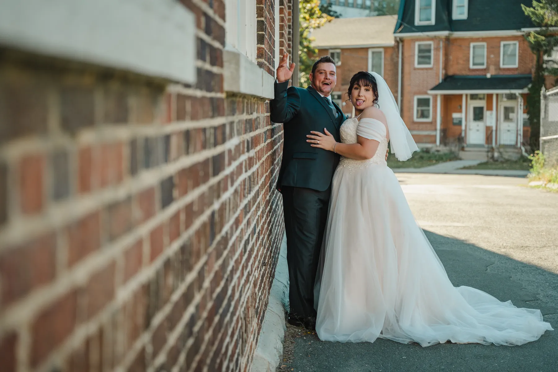 The couple embracing beside a brick building at Kody and Jaz’s wedding.