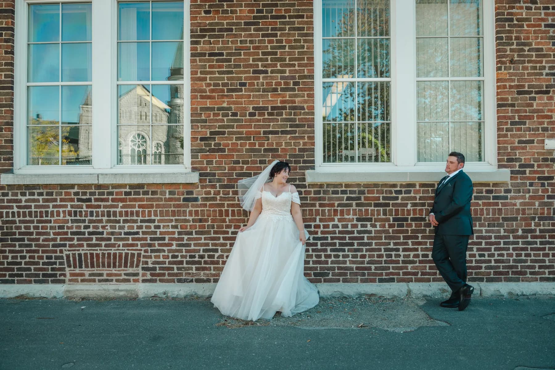 The couple walking and posing beside a brick wall at Kody and Jaz’s wedding.