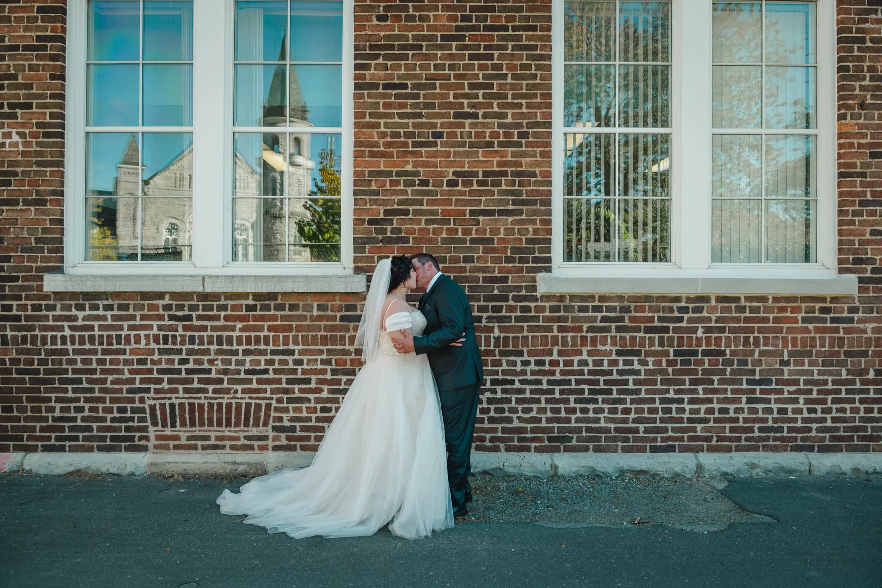 The couple walking and posing beside a brick wall at Kody and Jaz’s wedding.