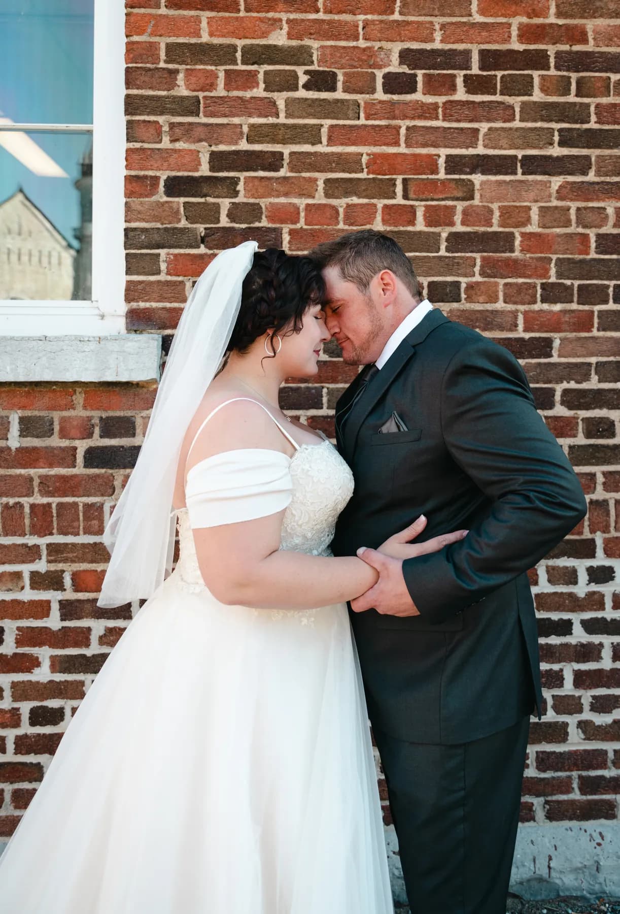 The couple walking and posing beside a brick wall at Kody and Jaz’s wedding.