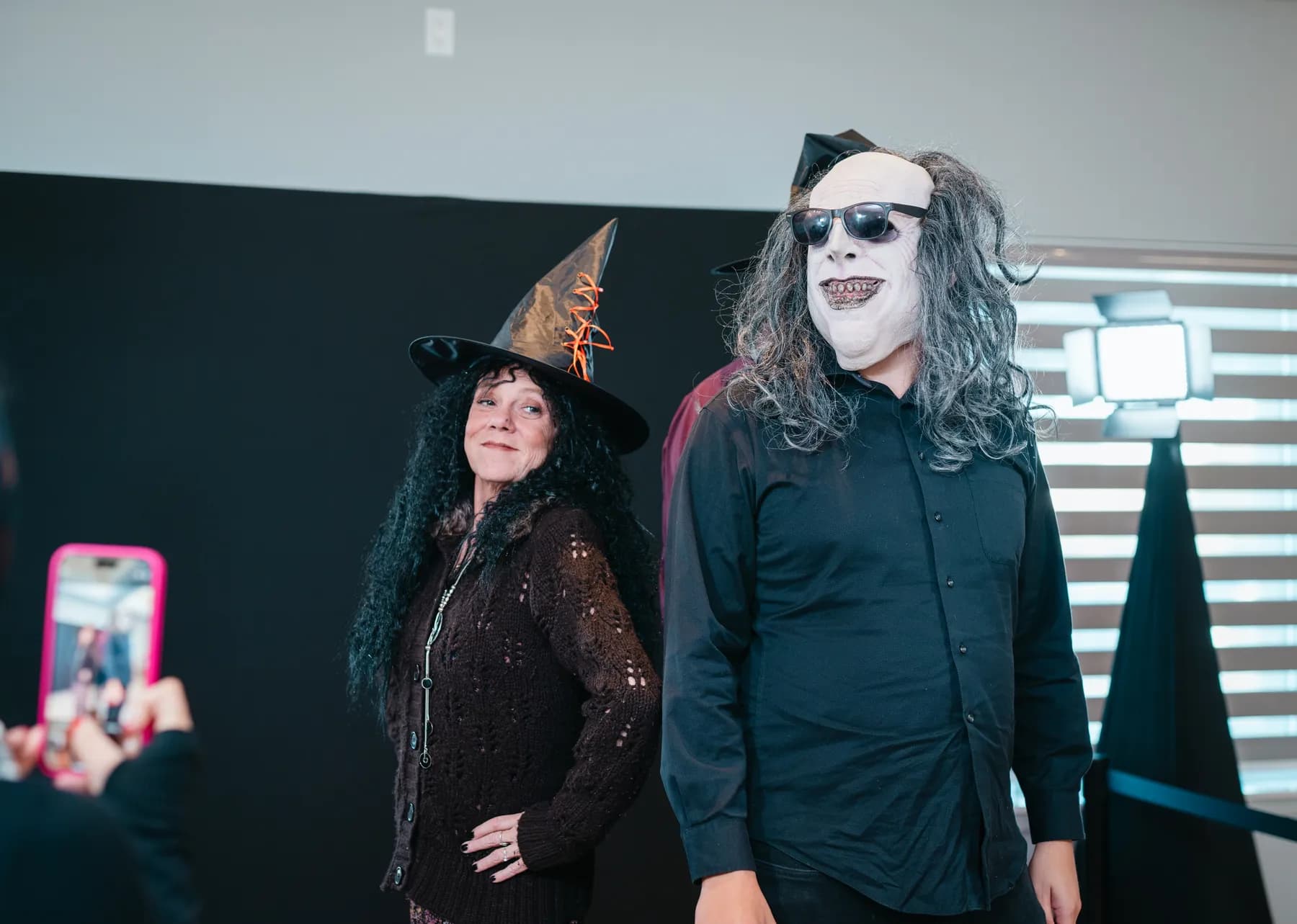 Costumed guests posing in front of a dark photo backdrop at Jenna and Jake’s Halloween party.