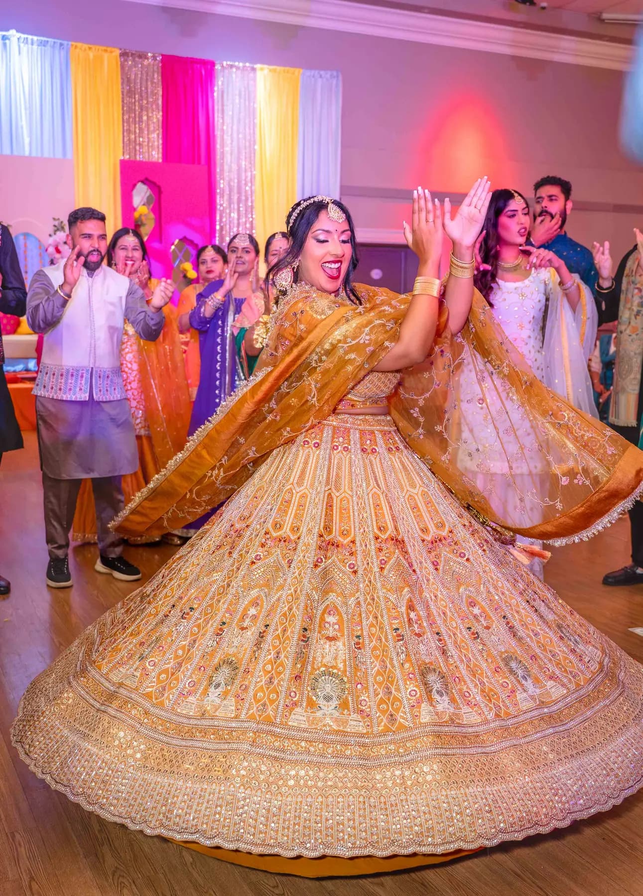 A woman dancing in a gold outfit at Jessie and Erin’s Haldi celebration.