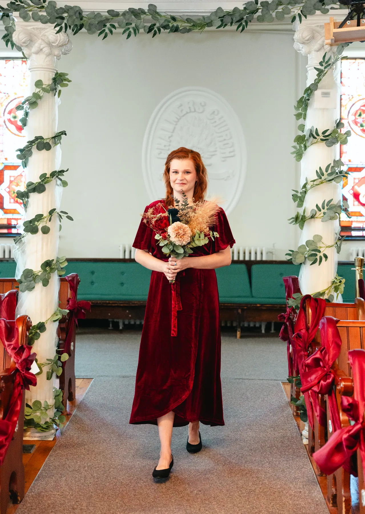 Bridesmaids in burgundy dresses with bouquets inside the church at Kody and Jaz’s wedding.
