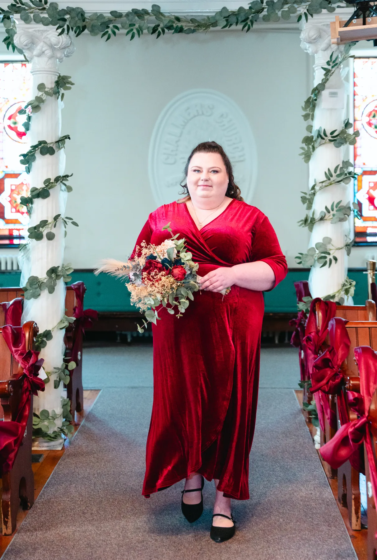 Bridesmaids in burgundy dresses with bouquets inside the church at Kody and Jaz’s wedding.