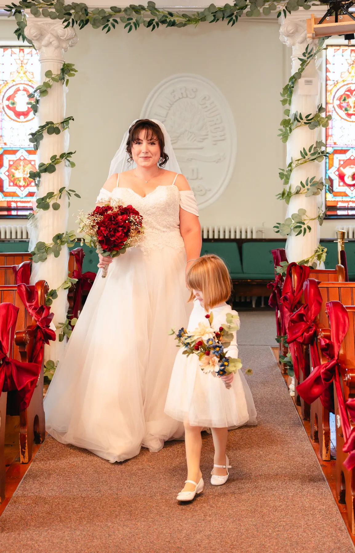 The bride with a flower girl at the front of the church at Kody and Jaz’s wedding.
