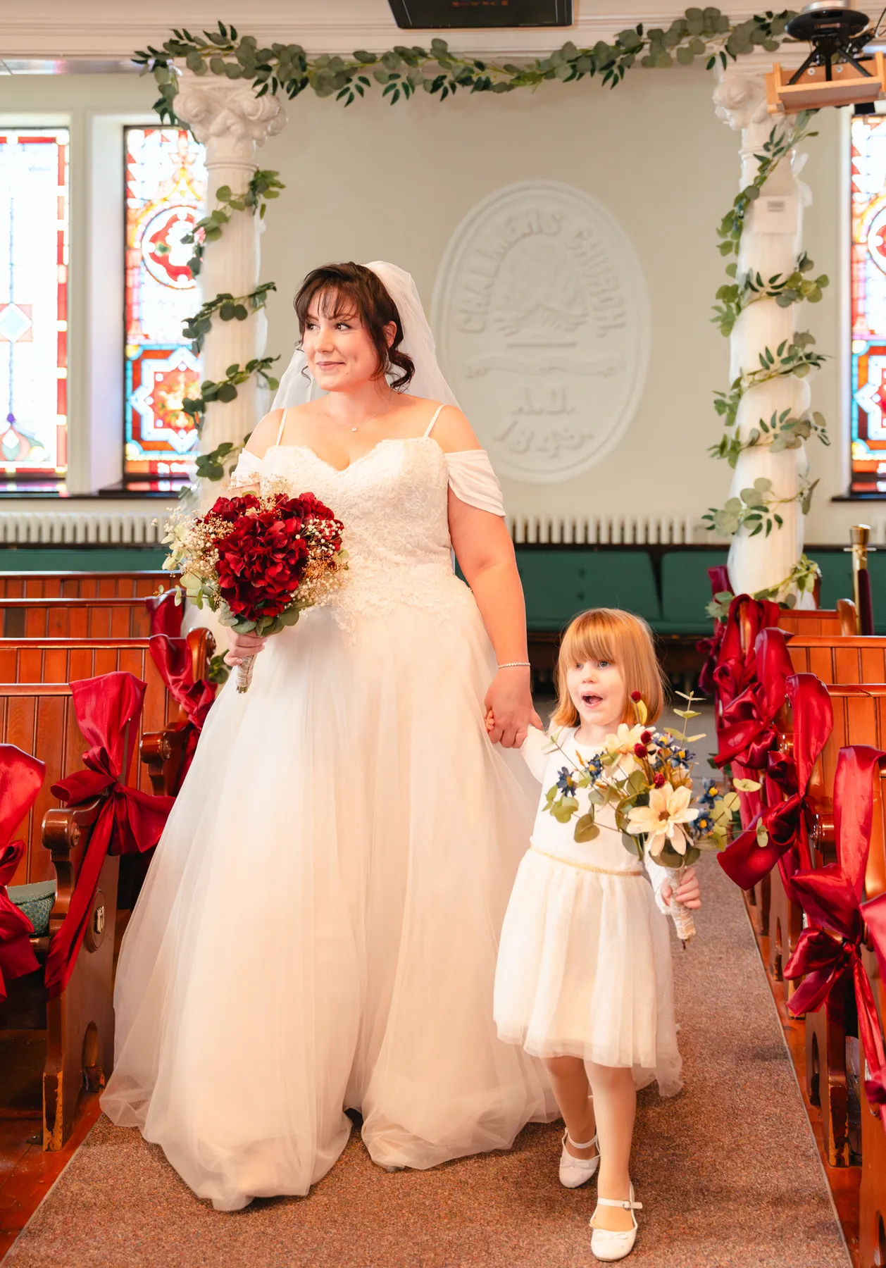 The bride with a flower girl at the front of the church at Kody and Jaz’s wedding.