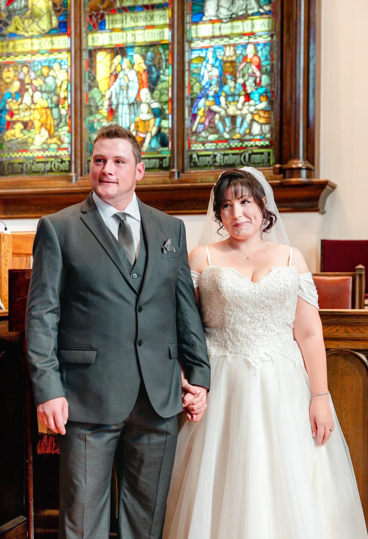 The newly married couple beside stained glass windows at Kody and Jaz’s wedding.