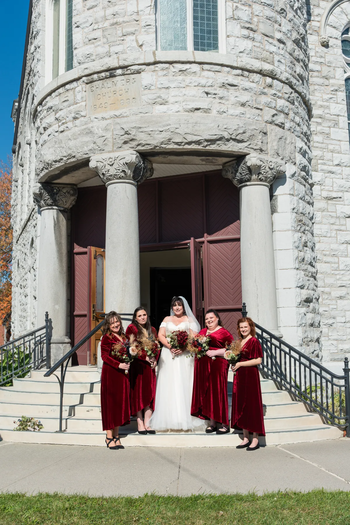 The bride with bridesmaids and a flower girl outside the church at Kody and Jaz’s wedding.