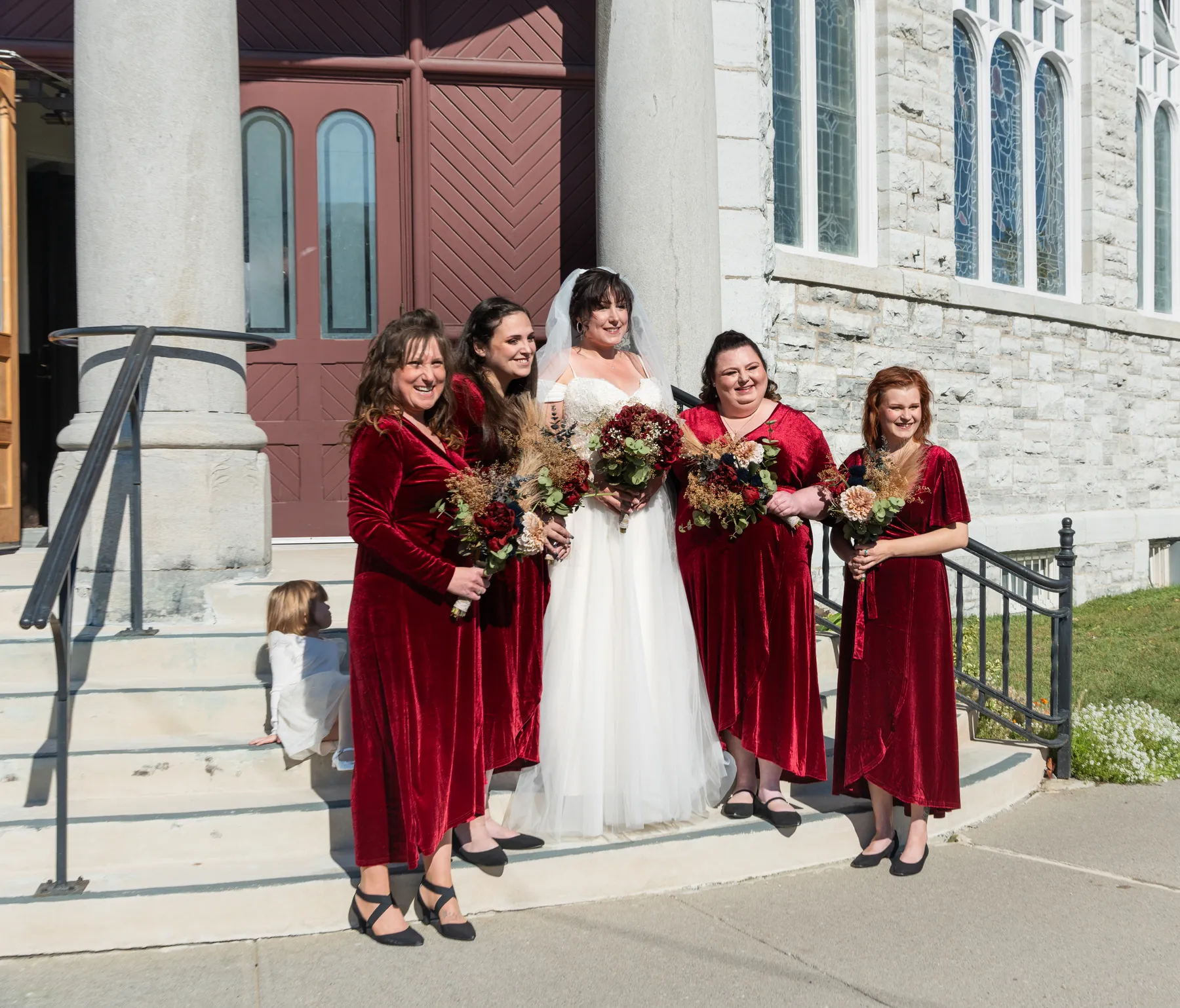 The bride with bridesmaids and a flower girl outside the church at Kody and Jaz’s wedding.