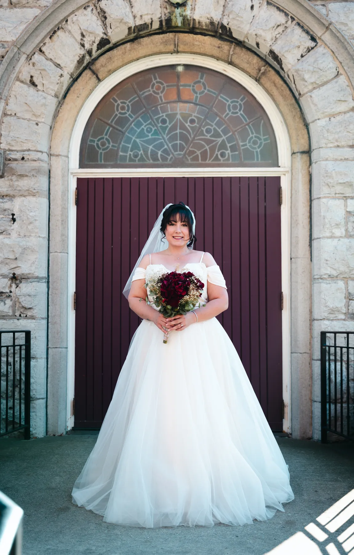 The bride posing at the red church door at Kody and Jaz’s wedding.