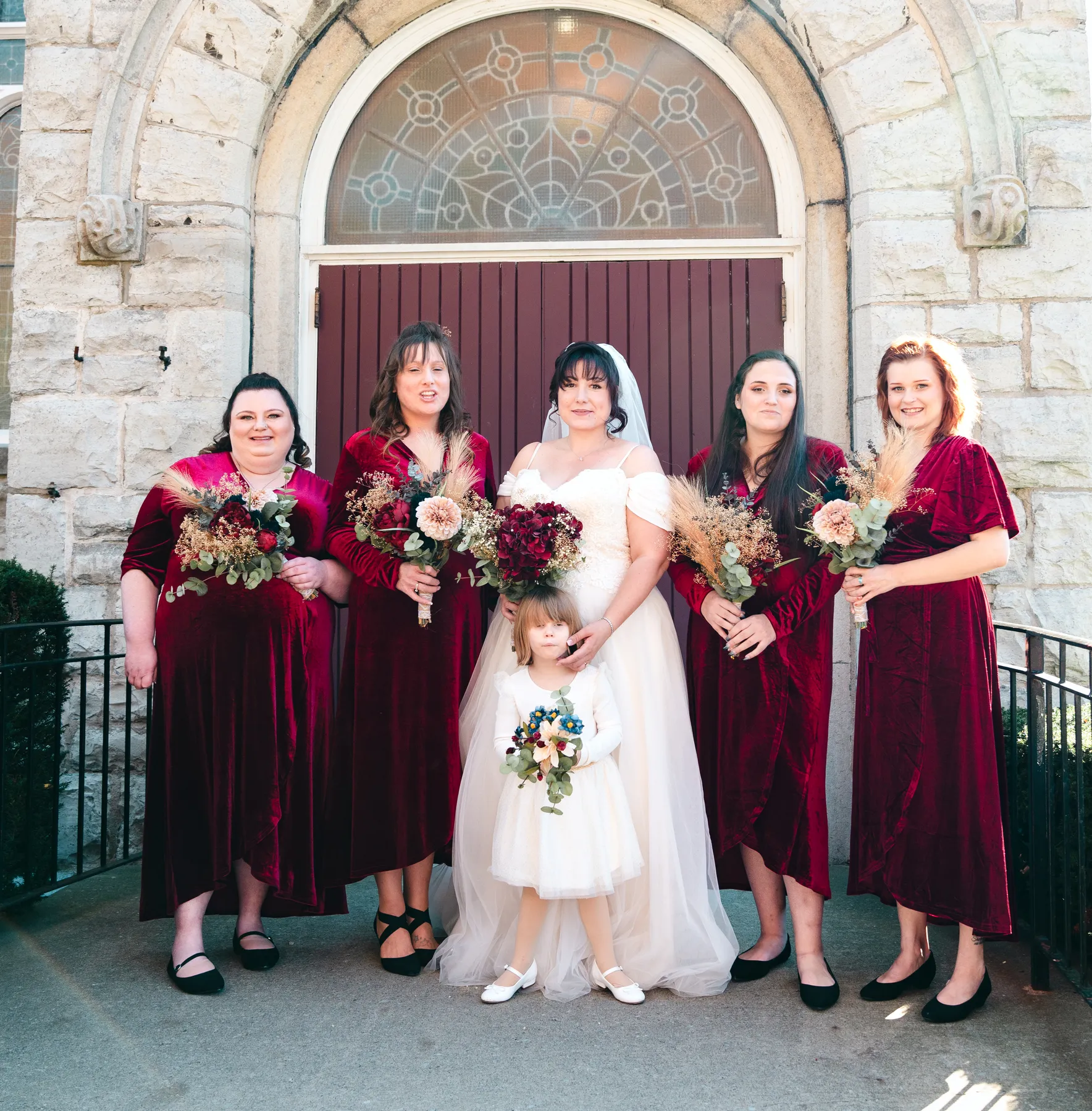 The bride with bridesmaids and a flower girl at the church door at Kody and Jaz’s wedding.
