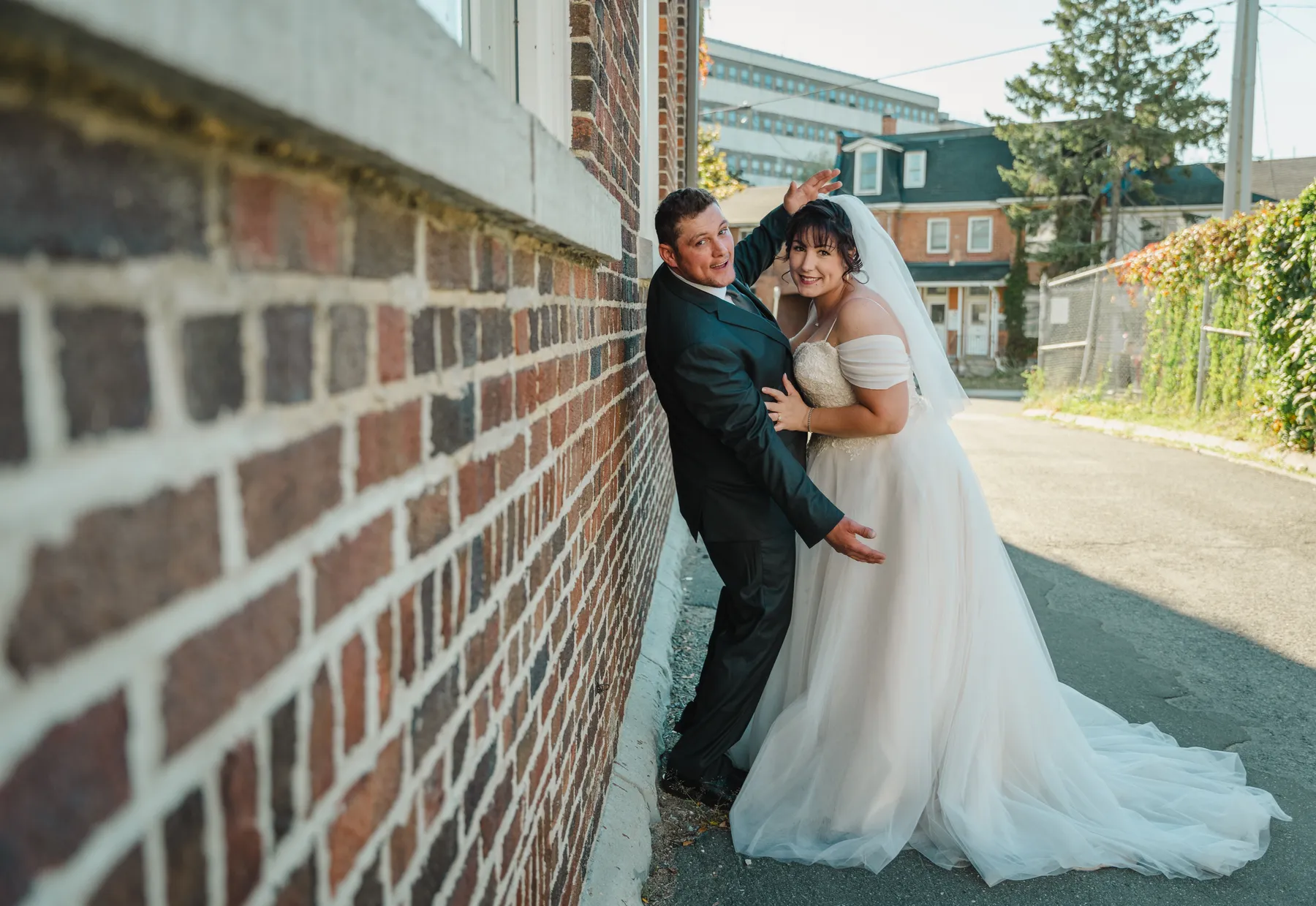 The couple embracing beside a brick building at Kody and Jaz’s wedding.