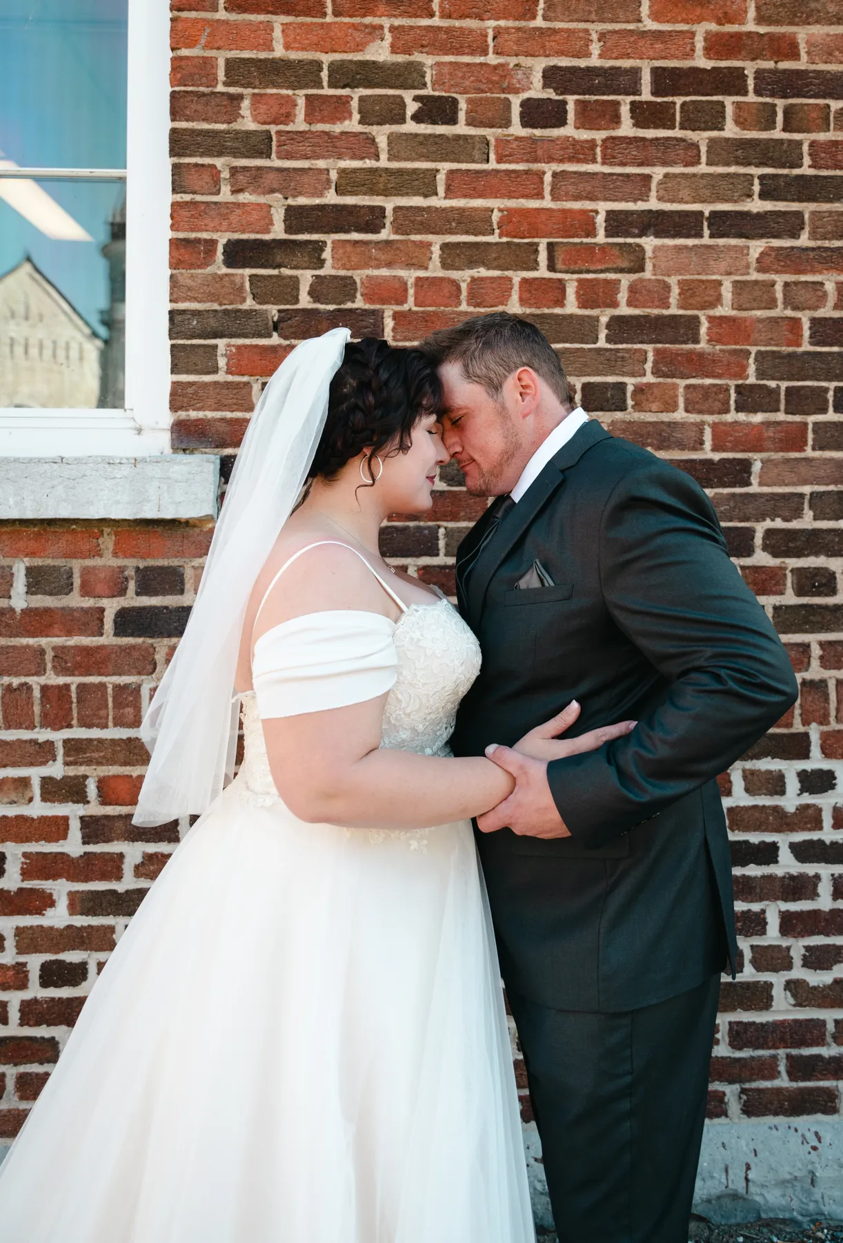 The couple walking and posing beside a brick wall at Kody and Jaz’s wedding.
