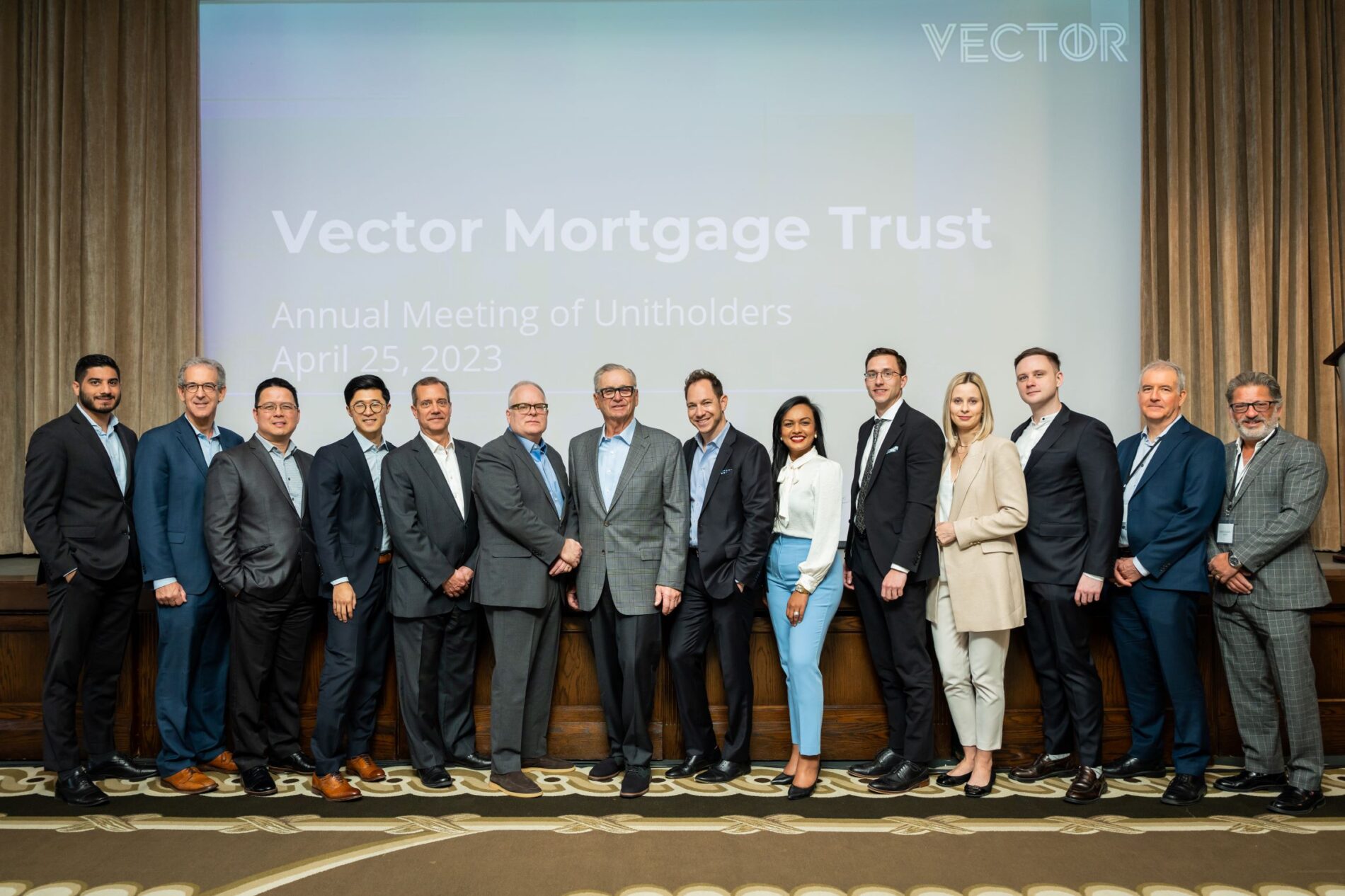 Group of attendees at the Vector Mortgage Trust Annual Meeting of Unitholders on April 25, 2023, in front of a branded backdrop, captured by Ghalib Ahmad, Winnipeg event photographer.